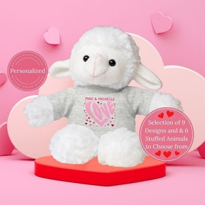 May include: A white plush lamb wearing a gray shirt with a pink heart and the text "MIKE & MICHELLE LOVE" printed on it. The lamb is sitting on a red heart-shaped base.  Selection of 9 Designs and 6 Stuffed Animals to Choose from.