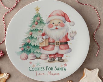 Puede incluir: Plato de cerámica blanco con una ilustración de acuarela de Santa Claus sosteniendo un regalo y de pie junto a un árbol de Navidad. El plato tiene el texto "Cookies for Santa Love, Mason" impreso en él.