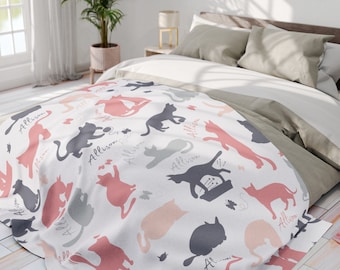 Könnte beinhalten: Eine weiße Decke mit Katzen-Silhouetten in Grau-, Rosa- und Pfirsichtönen. Der Name "Allison" ist in Schreibschrift auf dem Design geschrieben. Die Decke liegt auf einem Bett mit neutralfarbener Bettwäsche.