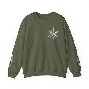 May include: A green sweatshirt with a white snowflake design on the front and white snowflakes on the sleeves.