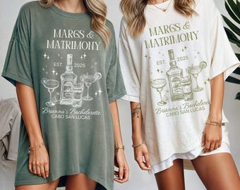 Puede incluir: Dos mujeres con camisetas de gran tamaño con el texto "MARGS & MATRIMONY EST. 2025" y un gráfico de una botella de tequila y vasos de margarita. El texto "Brianna's Bachelorette CABO SAN LUCAS" también está en las camisetas.