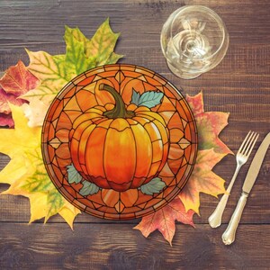 Puede incluir: Un plato de vidrio coloreado con un dise&ntilde;o de calabaza. El plato est&aacute; rodeado de hojas de oto&ntilde;o en tonos de rojo, naranja y amarillo. El plato est&aacute; sobre una mesa de madera.