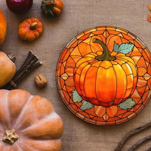 Puede incluir: Un dise&ntilde;o de calabaza de vitral en un plato redondo de madera. La calabaza es naranja con un tallo y hojas verdes. El plato tiene un marco de madera marr&oacute;n y est&aacute; rodeado de decoraciones de oto&ntilde;o.