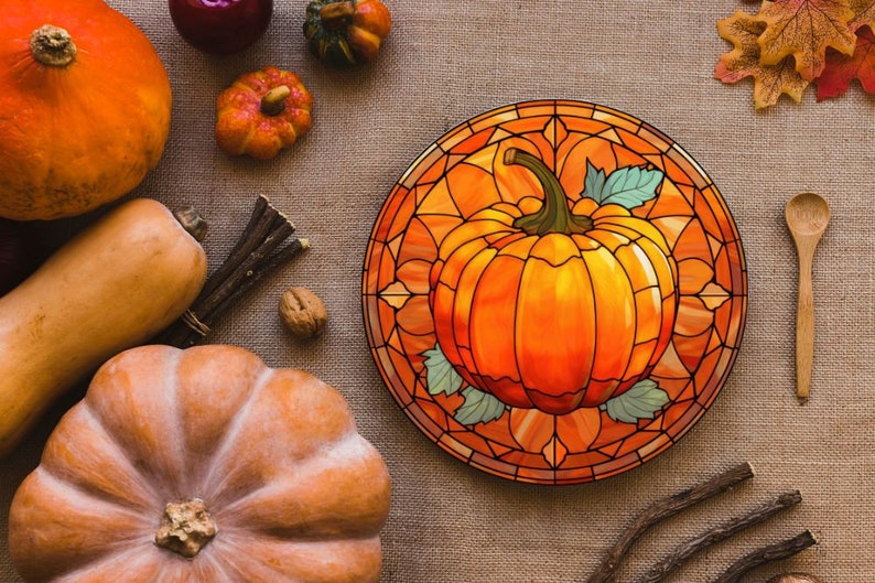 Puede incluir: Un dise&ntilde;o de calabaza de vitral en un plato redondo de madera. La calabaza es naranja con un tallo y hojas verdes. El plato tiene un marco de madera marr&oacute;n y est&aacute; rodeado de decoraciones de oto&ntilde;o.