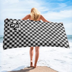Peut inclure: Une serviette de plage à carreaux noirs et blancs avec un cercle noir contenant un symbole stylisé au centre.