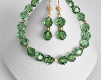 May include: A green crystal bead bracelet and matching earrings set. The bracelet is made with faceted green crystal beads and gold-toned spacers. The earrings are dangle style with two green crystal beads on each earring.