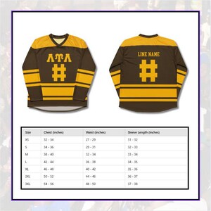 Op de afbeelding: Bruin en goudkleurig shirt met lange mouwen met de letters "ATA" en een hekjesymbool op de voorkant. De achterkant van het shirt heeft een hekjesymbool en ruimte voor een lijnnaam. Een maattabel met borst-, taille- en mouwmaten in cm is inbegrepen.