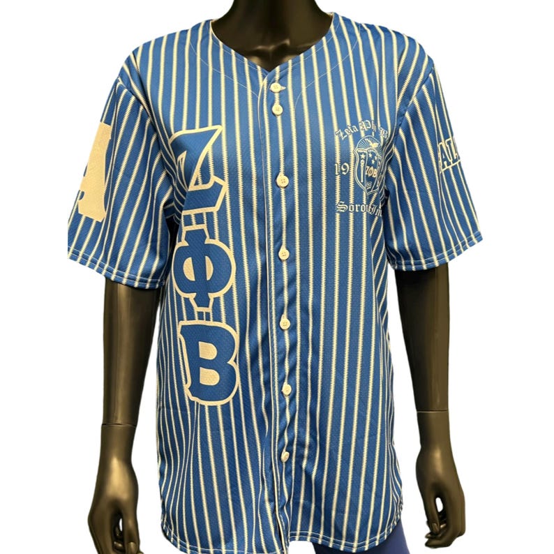 Puede incluir: Una camiseta de b&eacute;isbol a rayas azules y blancas con las letras "Z", "Phi" y "B" en el lado izquierdo. El lado derecho de la camiseta tiene un escudo con el texto "Zeta Phi Beta Sorority, Inc. 1920".
