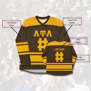 Op de afbeelding: Bruin en goudkleurig shirt met lange mouwen en een V-hals. Het shirt heeft de Griekse letters &Lambda;&Tau;&Lambda;, een hashtag-symbool en strepen op de mouwen. Een kleiner shirt is erachter zichtbaar, met hetzelfde ontwerp.