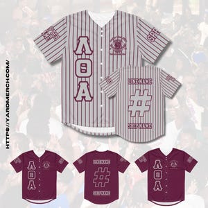 Può includere: Una maglia da baseball bianca e bordeaux con un motivo a righe sottili. La maglia ha le lettere "AOA" sul davanti e il numero "100" sulla manica. Il retro della maglia ha un segno di numero e il testo "LINE NAME" e "SHIP NAME".
