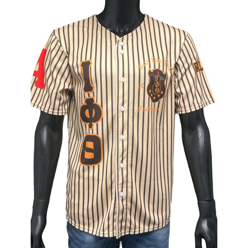 Puede incluir: Una camiseta de b&eacute;isbol a rayas beige y negras con un gran gr&aacute;fico naranja y negro "I &Phi; D" en el lado izquierdo. La camiseta tiene un frente abotonado blanco y un peque&ntilde;o escudo negro y dorado con el texto "Beta Phi Sigma 1919 Founded" en el lado derecho.