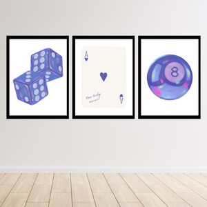 May include: Three framed prints featuring game-related imagery. One print shows two blue dice, another displays an Ace of Hearts playing card with the text "How lucky are we?", and the third depicts a purple eight ball.