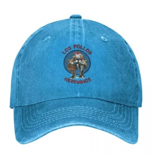 May include: A blue denim baseball cap with a distressed look. The front of the cap features a circular embroidered patch with the text "Los Pollos Hermanos" and a cartoon image of two chickens.