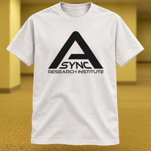 May include: A white short-sleeved t-shirt featuring a black graphic on the chest. The graphic displays a large letter A above the word SYNC and the text RESEARCH INSTITUTE in a clean, sans-serif font. The shirt has a crew neckline.