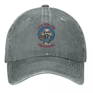 May include: A gray distressed denim baseball cap with a vintage-style embroidered logo featuring two chickens and the text "Los Pollos Hermanos".