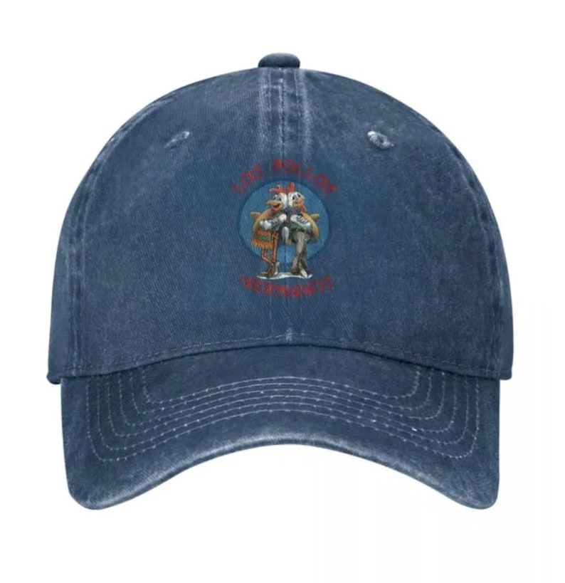 May include: A blue denim baseball cap with a distressed look. The cap features a circular patch with a cartoon image of two birds holding a fish. The text "Los Pollos Hermanos" is printed in red on the patch.