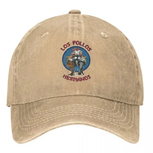 May include: A tan baseball cap with a distressed look. The front of the cap features a circular patch with the text "Los Pollos Hermanos" in red and blue lettering. Inside the circle is a cartoon image of two chickens.