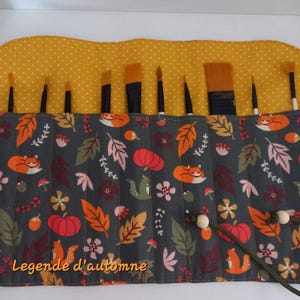 Peut inclure: Un étui enroulable en tissu gris avec une doublure jaune à pois. L'étui est imprimé d'un motif d'automne avec des citrouilles orange, des écureuils bruns et des renards roux. L'étui est conçu pour contenir des pinceaux et se ferme avec un cordon. Le texte "Legende d'automne" est imprimé sur le devant de l'étui.