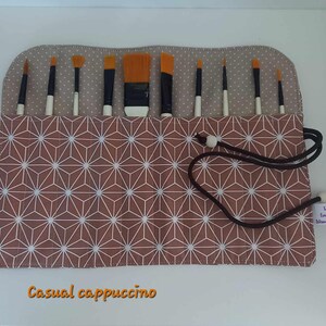 Peut inclure: Un rouleau en tissu à motif brun et blanc avec une fermeture à cordon. Le rouleau est conçu pour contenir des pinceaux et porte une étiquette indiquant "Talisman Cosmétiques Minimalist Moments".