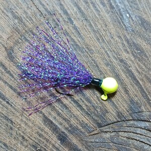 May include: A purple and iridescent fishing jig with a yellow bead and a black hook.