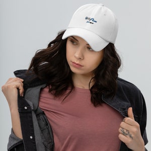 Op de afbeelding: Een witte baseballcap met de tekst "OnlyPlans jerag.w" in blauw script. De cap heeft een gebogen klep en een klassiek zes-panelen ontwerp. De hoed is gemaakt van een zacht materiaal.