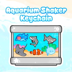 May include: An aquarium-themed keychain with the text "Aquarium Shaker Keychain." The keychain features cartoon illustrations of various sea creatures, including a blue spotted fish, a gray shark, a stingray, and an orange clownfish, all within a rectangular frame.