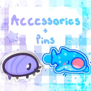 May include: Two cartoon pins or accessories are displayed. One is a purple oval with a white border, and the other is a blue fish-like character with a pink belly. The text "Accessories + Pins" is written above.