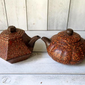 May include: Two brown teapots with a marbled pattern. One teapot has a geometric shape and the other has a rounded shape.