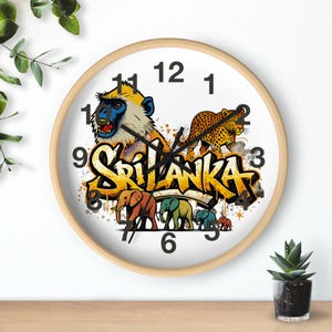 May include: Round wall clock with a light wood frame. The clock face features a colorful illustration of a monkey, leopard, and elephants, with the word "SRI LANKA" in graffiti style. Black clock hands and numerals.