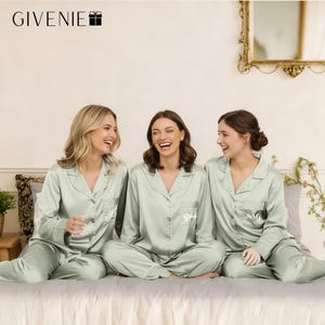May include: Three women wearing matching sage green satin pyjamas with white trim. The pyjamas have a button-down top and trousers. The middle top says "Bride" in white script. The other tops have initials. The brand name "GIVENIE" is at the top.