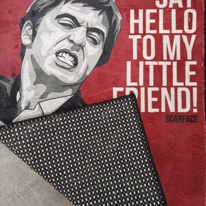 May include: A red doormat with a black and white illustration of a man's face and the text "Say hello to my little friend!"  Scarface is printed in smaller text below the illustration.