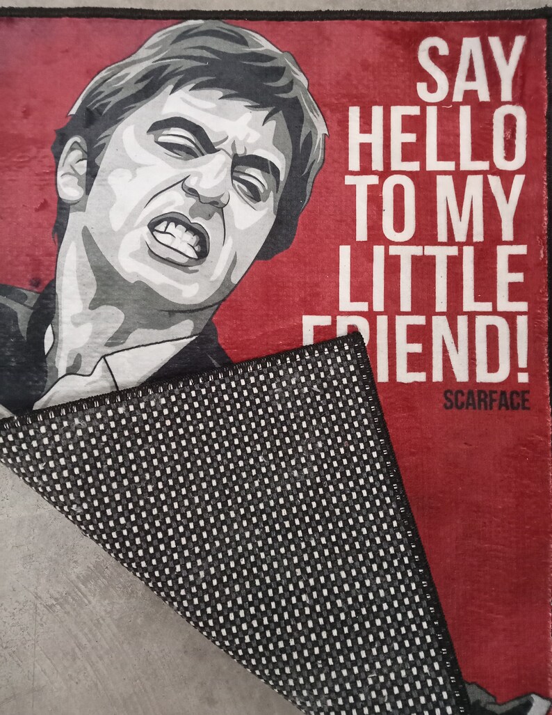 May include: A red doormat with a black and white illustration of a man's face and the text "Say hello to my little friend!"  Scarface is printed in smaller text below the illustration.