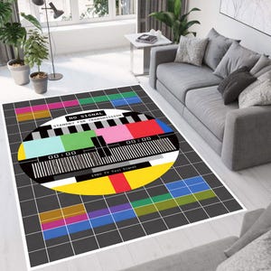 May include: A rectangular area rug featuring a retro TV test signal design. The rug has a black background with a grid pattern and a large, colorful test pattern in the center. The text "NO SIGNAL STANDBY FOR TRANSMISSION" is visible.