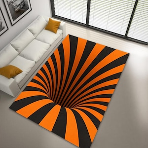 May include: A rectangular rug with a black and orange spiral design, creating a 3D optical illusion. The rug features alternating black and orange curved stripes radiating from a central point, giving the impression of a hole.