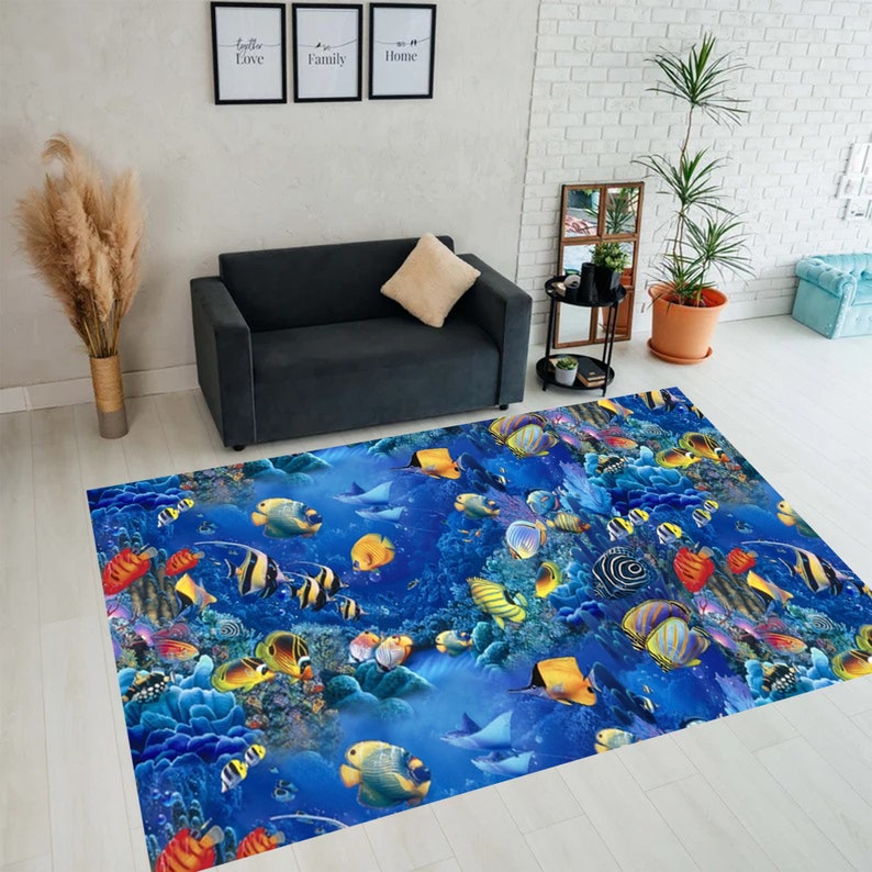 May include: A rectangular area rug featuring a vibrant underwater scene with colorful fish, coral, and rays against a deep blue background. The rug is placed on a light-colored wooden floor, with a dark gray sofa and decorative elements in the background.