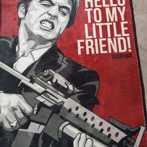 May include: A red and black poster with a man holding a gun. The text on the poster says "Say hello to my little friend! Scarface".