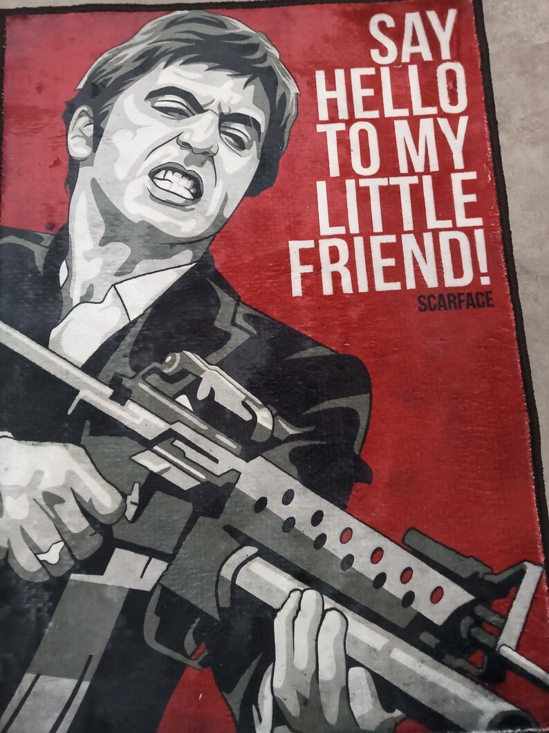 May include: A red and black poster with a man holding a gun. The text on the poster says "Say hello to my little friend! Scarface".