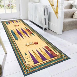 Op de afbeelding: Een rechthoekig tapijt met een backgammon-thema, met een beige achtergrond en een kleurrijke rand. Het tapijt heeft de driehoekige punten van het spel in paars en geel, met blauwe en bruine speelstukken en dobbelstenen.