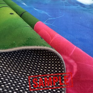May include: Rolled-up rug with a koi fish design. The rug features a vibrant color palette, including shades of green, pink, and blue. The underside of the rug has a black and white checkered pattern. The word "SAMPLE" is stamped on the rug.