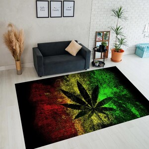 Pode incluir: Tapete retangular com um desenho de folha de cannabis. O tapete tem um fundo preto com um gradiente de cores vermelho, amarelo e verde. É colocado sobre um chão de madeira clara, numa sala de estar.