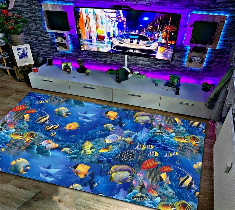 May include: A rectangular area rug featuring a vibrant underwater scene with colorful fish, coral, and a blue ocean backdrop. The rug is placed in a room with a large TV, a white entertainment center, and a brick wall.
