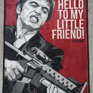 May include: A black and white illustration of a man holding a gun. The background is red and the text "SAY HELLO TO MY LITTLE FRIEND! SCARFACE" is printed on the right side of the image.