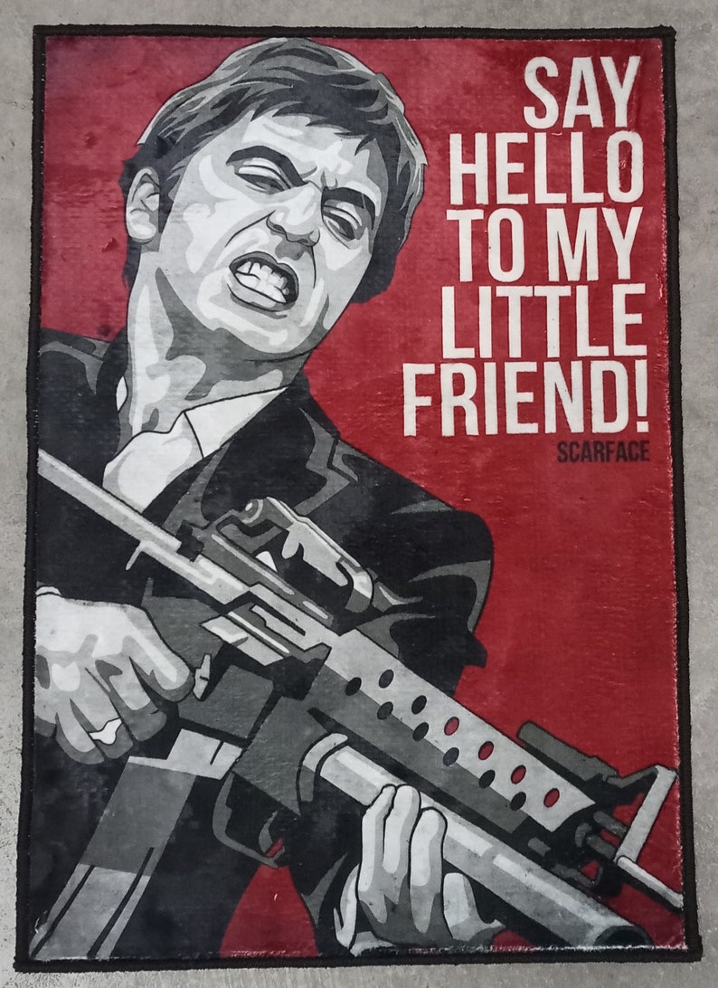 May include: A black and white illustration of a man holding a gun. The background is red and the text "SAY HELLO TO MY LITTLE FRIEND! SCARFACE" is printed on the right side of the image.
