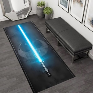 Könnte beinhalten: Eine schwarze und blaue Star Wars-Fußmatte mit einem Lichtschwert und dem Symbol der Rebellenallianz.