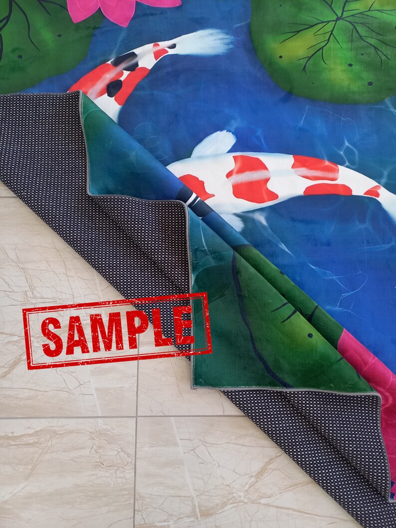 May include: A folded rug featuring a koi pond design with koi fish, lily pads, and a pink lotus flower. The rug has a blue, green, and white color scheme. The underside of the rug is black with white dots. The word "SAMPLE" is stamped on the rug.