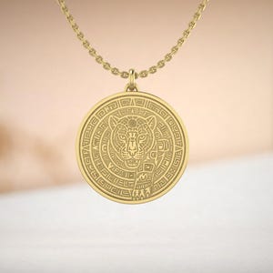 May include: A gold-colored pendant necklace featuring a circular pendant with an engraved jaguar design. The pendant is suspended from a delicate chain. The jaguar design is surrounded by intricate patterns.