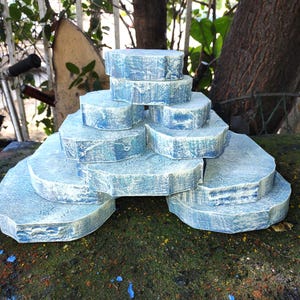 May include: A tiered, light blue decorative structure resembling a miniature rock formation. The levels are various sizes and shapes, with a textured surface and white highlights. The structure is designed to resemble a natural rock formation.
