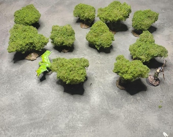 May include: A collection of ten miniature green trees with a green plastic dragon figurine on a gray surface.