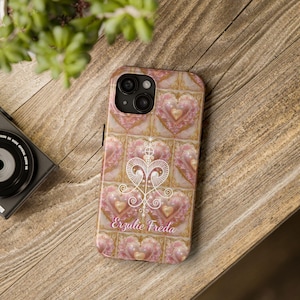 May include: A pink and gold phone case with a white design of a heart and the text "Erzulie Freda".