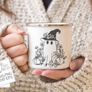 May include: A white enamel mug with a black and white illustration of a ghost wearing a witch hat with flowers. The ghost is surrounded by pumpkins and flowers.